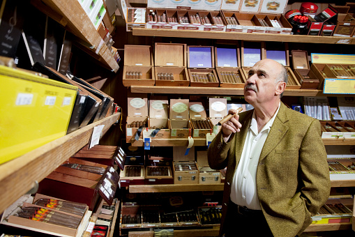 Small tobacco store owner looking at cigar boxes on display in shop