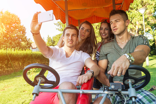 Four young people in a four-wheeled bicycle, they do selfie