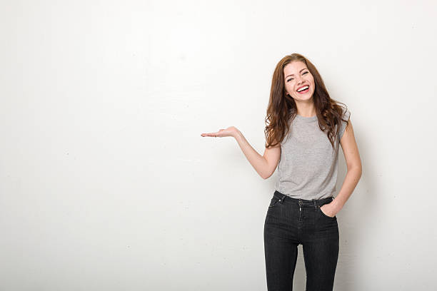 Happy Young Woman with White Wall and Casual Clothing Young woman in casual clothes, smiling, photographed against a slightly textured white wall with copy space to one side.  hand palm stock pictures, royalty-free photos & images