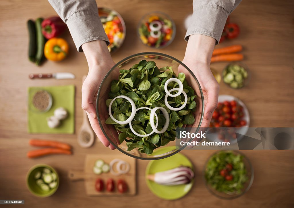 Healthy fresh homemade salad Hands holding an healthy fresh vegetarian salad in a bowl, fresh raw vegetables on background, top view 2015 Stock Photo