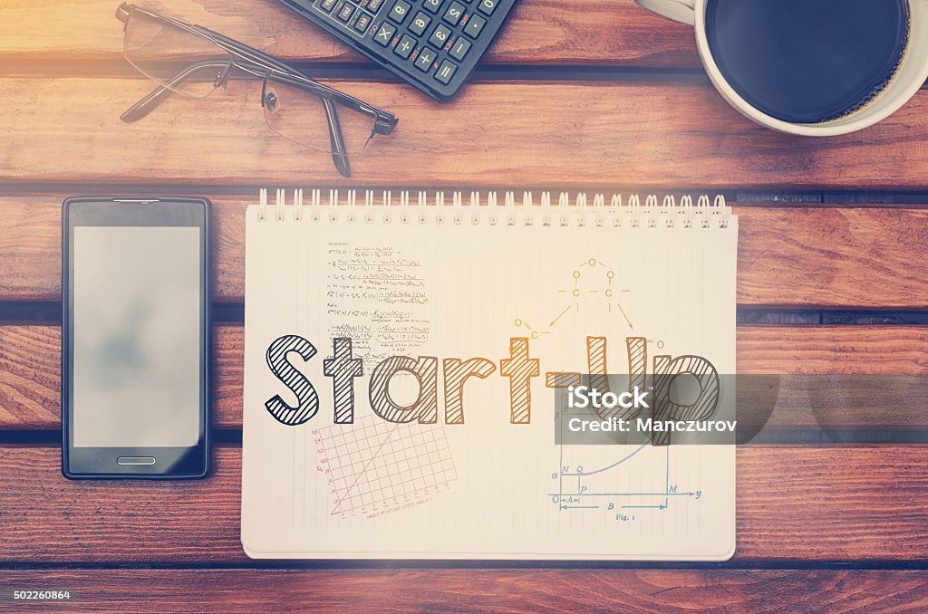 Notebook with text inside Start Up on table Notebook with text inside Start Up on table with coffee, mobile phone and glasses. 2015 Stock Photo