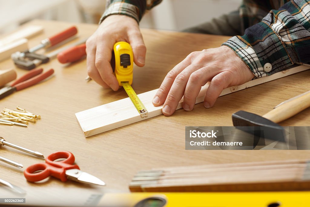 Man working on a DIY project Man working on a DIY project and measuring a wooden plank with work tools all around, hands close up Hand Tool Stock Photo