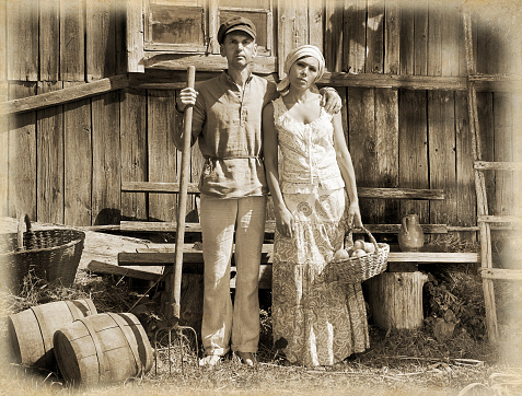 Couple in a stiff, old classic retro pose, standing in front of wooden stable.