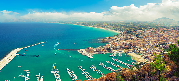 Italy, Sicily - Castellammare del golfo bay full of boats and yachts. Typical Sicilian architecture in the center of composition. Tyrrhenian sea and blue sky with clouds on the background. Shot from a viewpoint over the city. High resolution panorama, taken with Canon 5D mk III, toned and postprocessed in Photoshop for a warm summer look. Perfect image for magazines and web articles about Sicily.