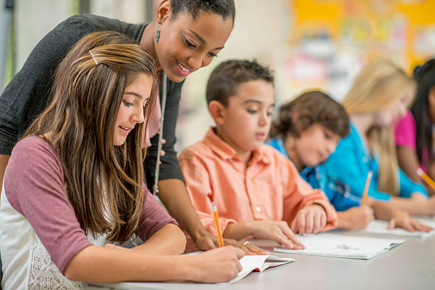 Getting Help on a Homework Question A multi-ethnic group of elementary children are sitting in class and are sitting at their desks are are taking a test. One student is getting some clarification on the test question. teachers stock pictures, royalty-free photos & images