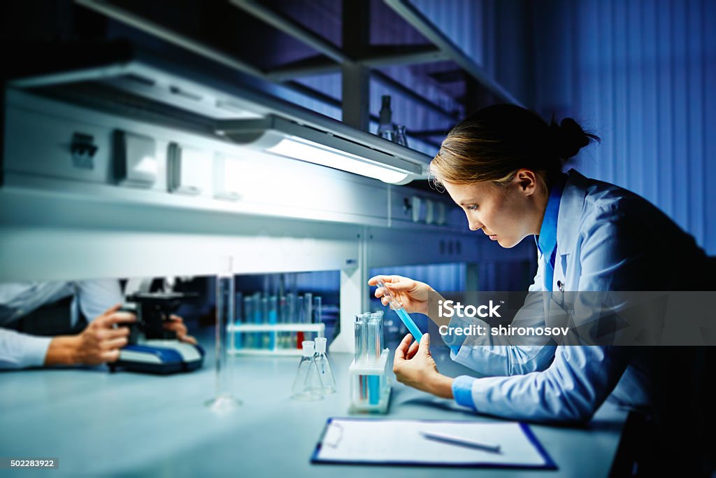 Studying virus Young lab worker looking at liquid in flask Laboratory Stock Photo