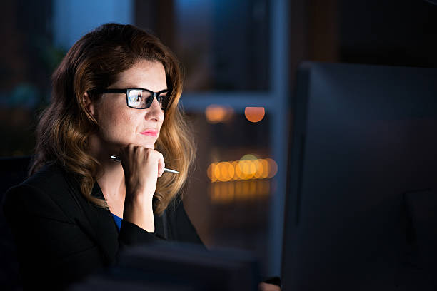 Reading important information Concentrated business lady reading information on glowing screen on her computer working late photos stock pictures, royalty-free photos & images