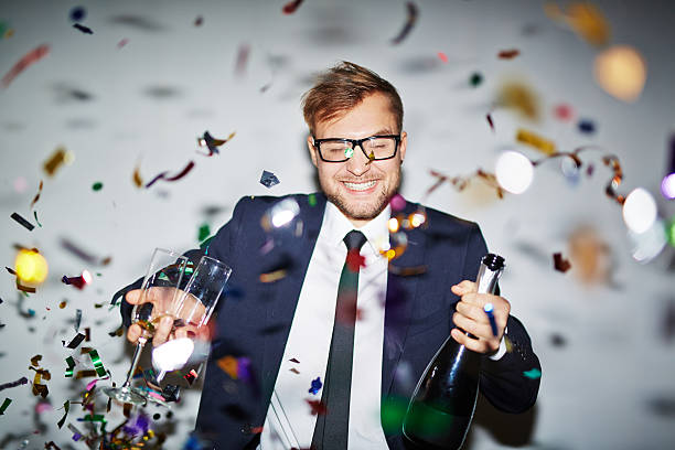 Businessman at party Happy businessman with bottle of champagne and two glasses standing under falling confetti office parties stock pictures, royalty-free photos & images