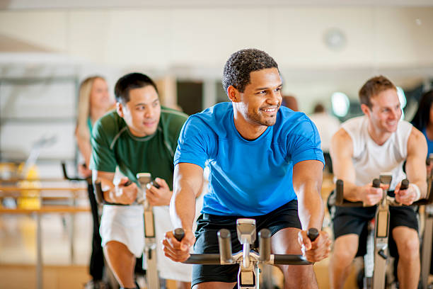 Fitness Class at the Gym A multi-ethnic group of young adults are working out at the gym by taking a cycling exercise class. community health center stock pictures, royalty-free photos & images