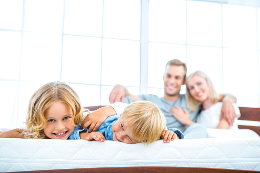 Photo of young family of four lying on nice white bed. Young family demonstrating quality of mattress