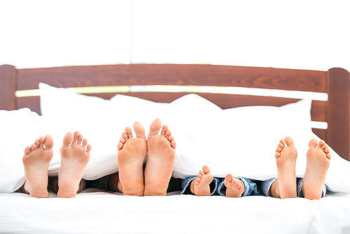 Photo of loving family of four lying on white bed in morning. Only legs are not under blanket