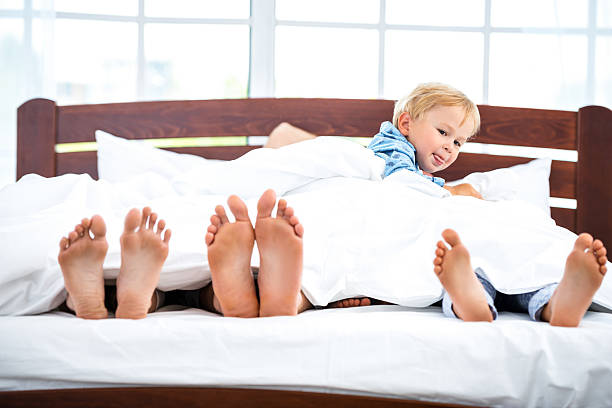 Young family on white bed Photo of loving family of four lying on white bed in morning. Only legs are not under blanket bed human foot couple two parent family stock pictures, royalty-free photos & images