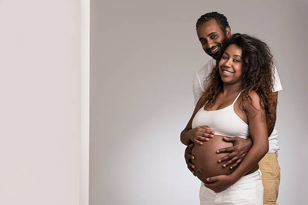 Attractive african american couple indoor. Young pregnant couple in their 8 months pregnancy, placing hand on woman's pregnant stomach. huge black woman pictures stock pictures, royalty-free photos & images