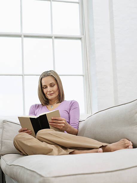istock Middle Aged Woman Reading Book On Sofa 502301247