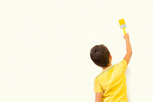 Little boy drawing something using painting brush on wall background