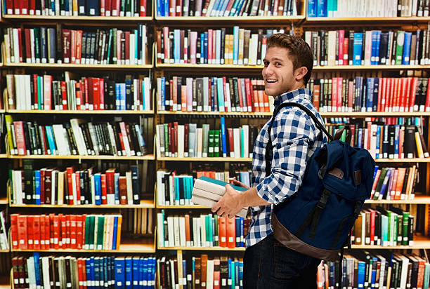 istock Smiling male student holding books in library 502319346