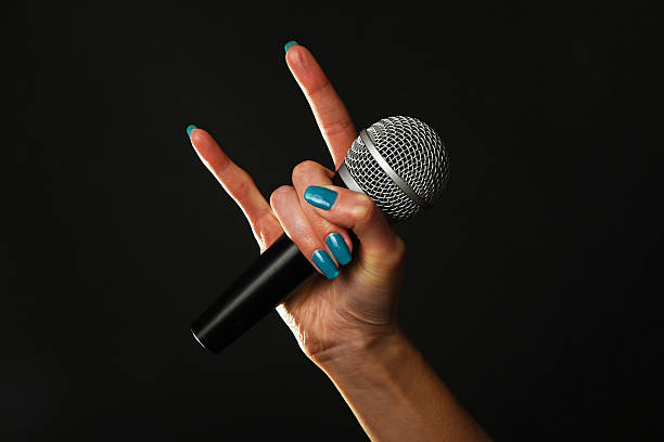istock Woman hand with microphone and devil horns isolated on black 502324240