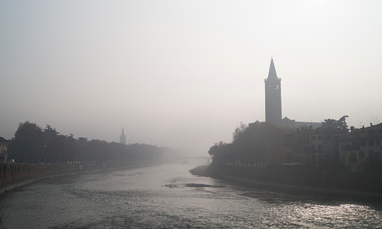 On photo foggy Verona, Italy from one of the bridges over the river Adige. Also on the city landscape is seen one of the towers of the city, all the photo made a silhouette