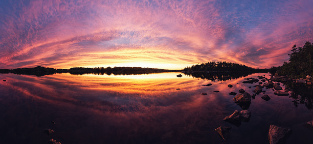 An intense sunset fills a still lake with colour. Panoramic view, stitched images.