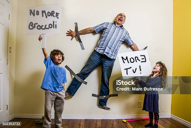 Kids Rebellion Led To Strapping The Father On Wall Stock Photo - Download Image Now - Child, Humor, Parent