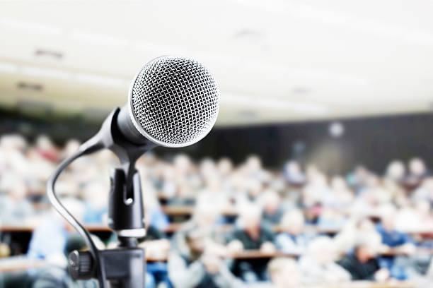 istock Large audience in auditorium with vocal mic await speaker 502376917