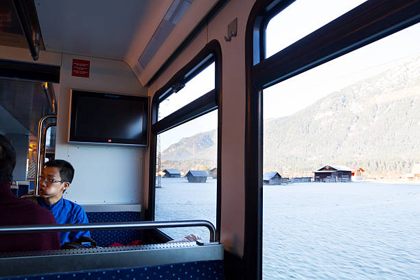 Garmisch-Patenkirchen, Germany - November 21, 2012: Capture inside of local train Zugspitzbahn in morning on way to Zugspitze. At left side are asian tourists. At right side are windows and outside are frosty meadows and barns. Young man is eating.