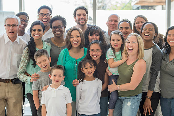 Multi-Generational Family Standing Together A multi-ethnic group of multi-generational families are standing together in a group and are smiling while looking at the camera. family reunion stock pictures, royalty-free photos & images