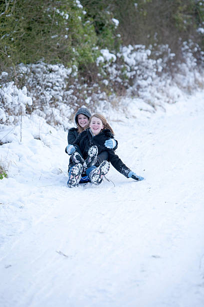 istock 2 girls laughing as they sledge  down a hill 502399836