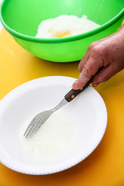 Hand with fork whiiping eggwhites in white small bowl, preparing fanesca concept.