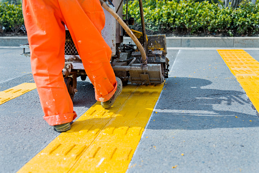 Pavement marker machine spraying yellow lines at a urban road.