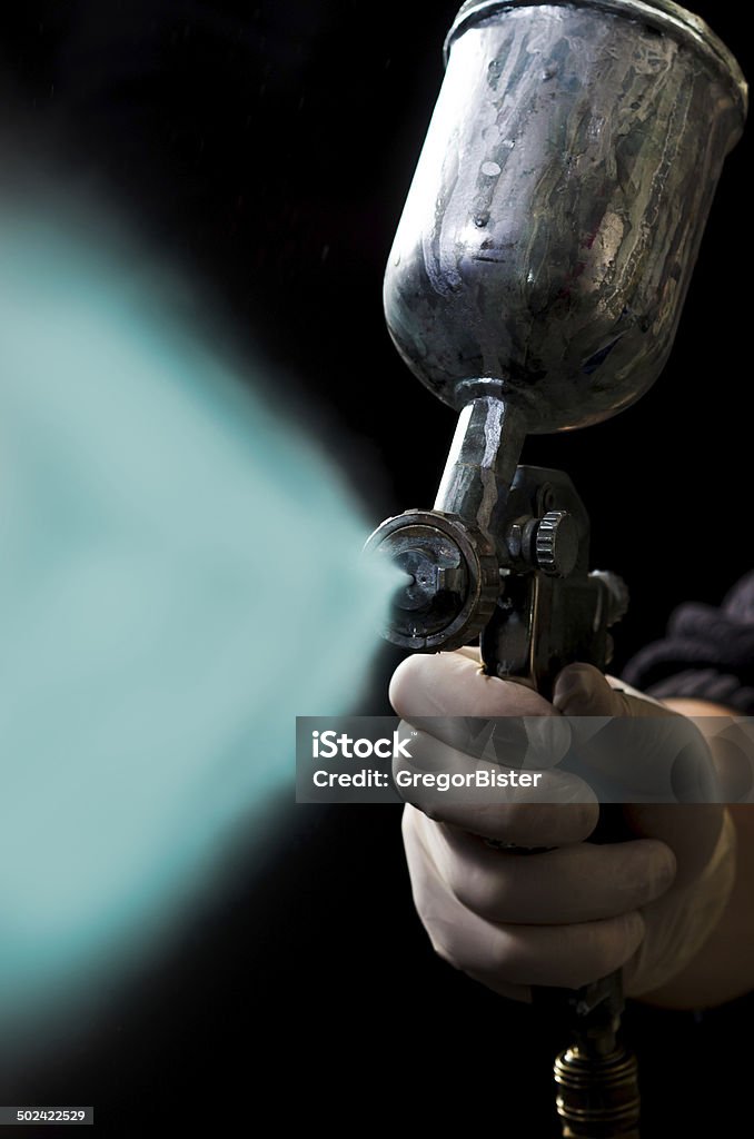 Spray gun in hand on dark background Painter painting with spray gun. Dark background. Adult Stock Photo