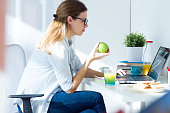 Pretty young woman eating an apple and working at home.