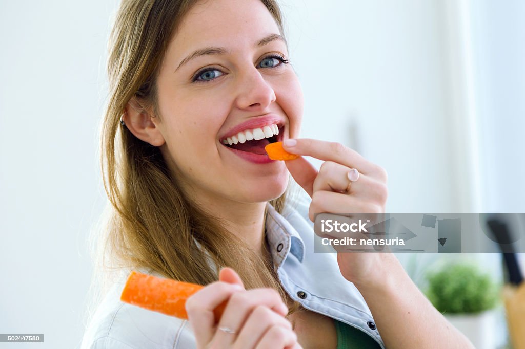 Pretty young woman eating carrot in the kitchen. Portrait of pretty young woman eating carrot in the kitchen. Carrot Stock Photo