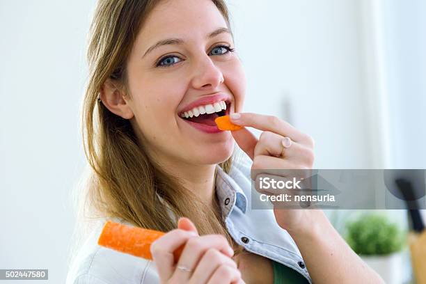 Foto de Bela Jovem Comendo Palitos Na Cozinha e mais fotos de stock de Cenoura - Cenoura, Comer, Mulheres