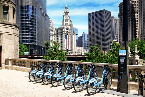 Chicago, USA - July 4, 2014: Divvy bicycle sharing system on State Street Bridge, downtown Chicago.  The Divvy system was launched in Chicago on June 28, 2013 with 750 bikes at 75 stations. Row of bikes for hire. Trump Tower, Wrigly Building with American Flag, Equitable Building, and some people in the background.