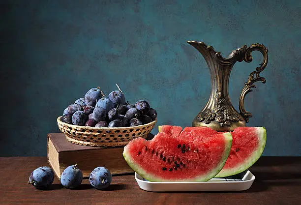 Watermelon slices and plums in wickerbasket on a wodden table