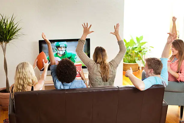 A group of cheering young people watching a football game together on TV. Image on TV screen is photographer's own.