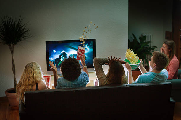 Group of Friends Watching Halloween Scary Movie Together at Home Group of young people in suspense watching a scary movie on TV together at home for Halloween. Image on TV screen is photographer's own. entertainment center stock pictures, royalty-free photos & images