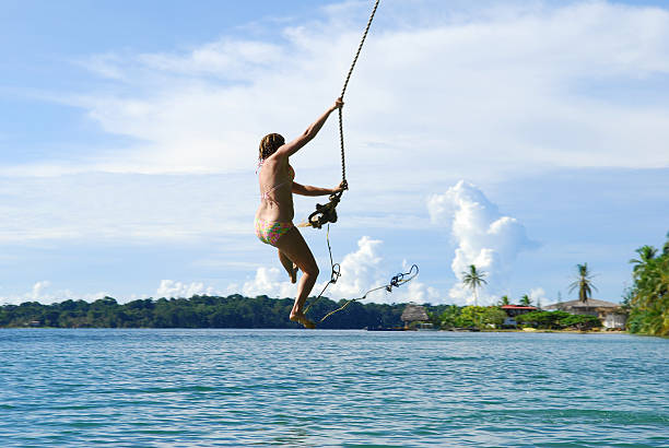 A young woman swings out from a palm tree to drop into the Caribbean Sea at Boca del Drago in Bocas del Toro, Panama