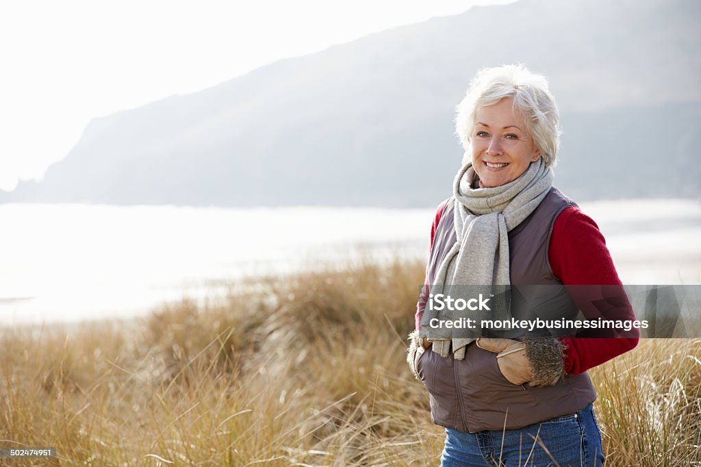 Senior mujer caminando a través de las dunas de arena en la playa de invierno - Foto de stock de Mujeres mayores libre de derechos
