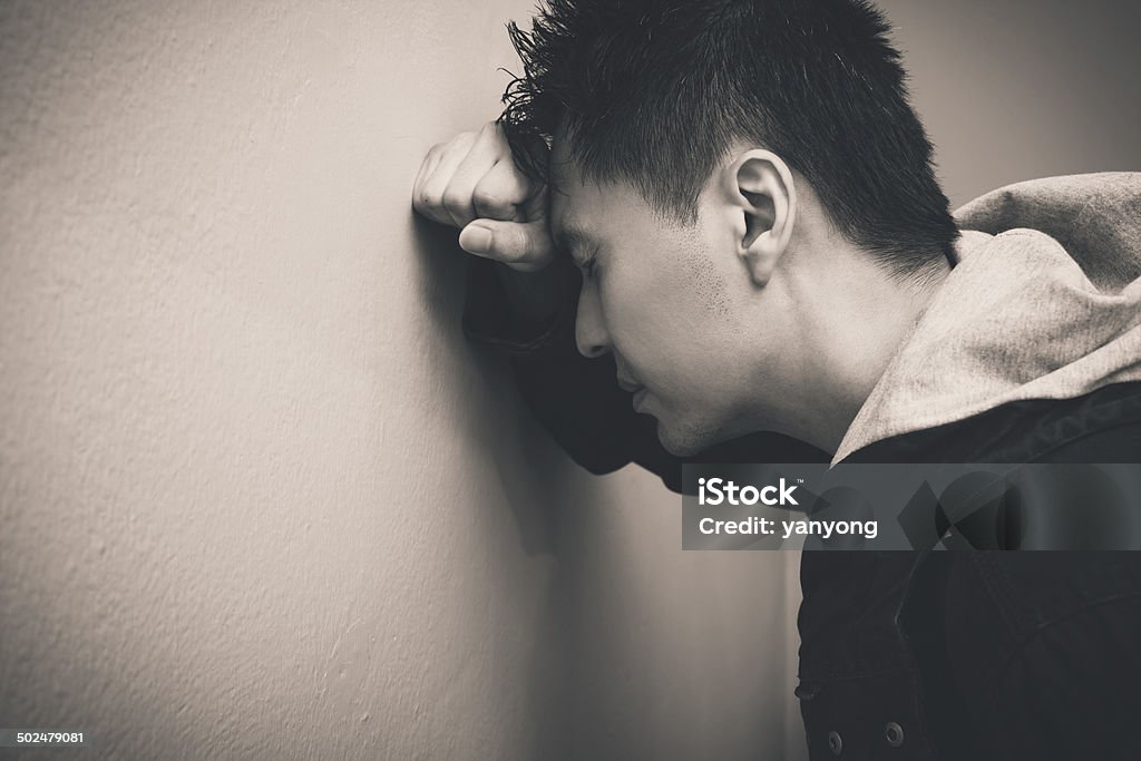 Depressed asian man Depressed asian man with fist clenched leaning his head against a wall Adult Stock Photo