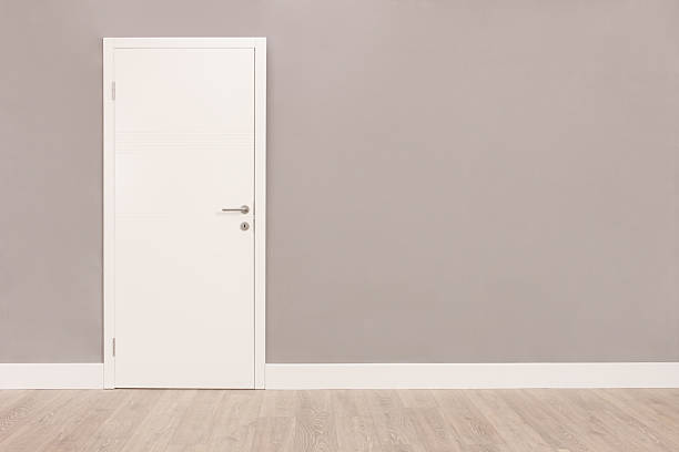 White door in an empty room Shot of a closed white door on a gray wall in an empty room doorway stock pictures, royalty-free photos & images