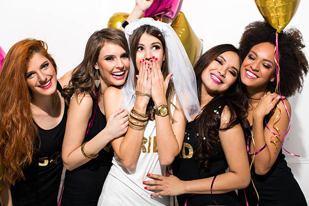 Bride's squad Young girlfriends celebrating bride night. Bride is wearing a veil and a T-shirt with the inscription ''BRIDE'', bridesmaids are wearing T-shirt with the inscription ''Squad''. They are laughing, dancing and singing.  Room is decorated with star and heart shaped balloons. bachelor stock pictures, royalty-free photos & images