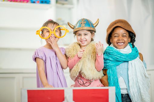 A multi-ethnic group of elementary age children are playing dress up together and are wearing costumes.