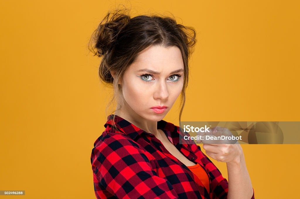 Angry irritated young woman in plaid shirt pointing on you Close up portrait of angry irritated young woman in plaid shirt pointing on you over yellow background 2015 Stock Photo