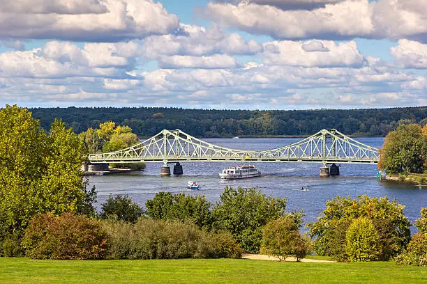 View to Glienicke Bridge, the Bridge of Spies. Glienicke Bridge is the bridge which spans the Havel River to connect the cities of Berlin and Potsdam. It was the bridge to exchange captured spies during the Cold War. The Bridge is also a symbol of German Reunification. Boats and the ships are moving at the River Havel.