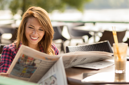 Beautiful young brunette sitting in a cafe, drinking coffee and reading newspapers