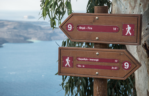 Signs along hiking path in Fira on the island of Santorini, Greece with the Aegean Sea in the background