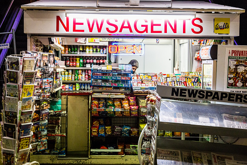 London, UK - December 21, 2015: an Asian female newspaper seller surrounded by her stock of confectionary and snacks in her kiosk on The Strand in central London, UK.