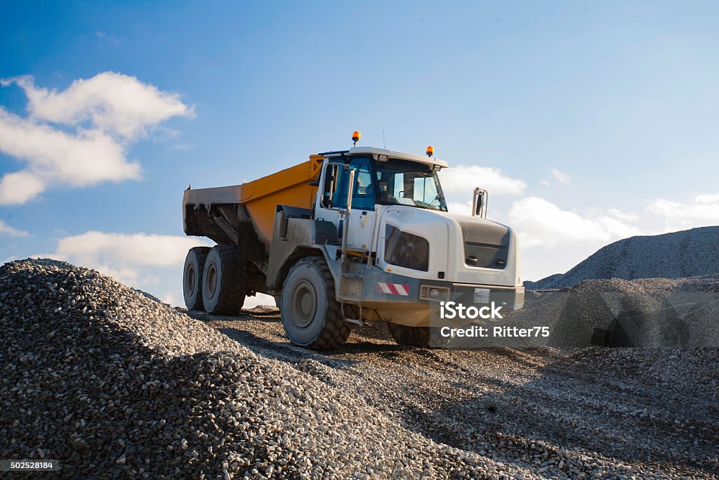 Dump Truck Driving Down the Gravel Hill Dump truck working on gravel pit is driving down the hill of gravel in sunny day. Quarry Stock Photo